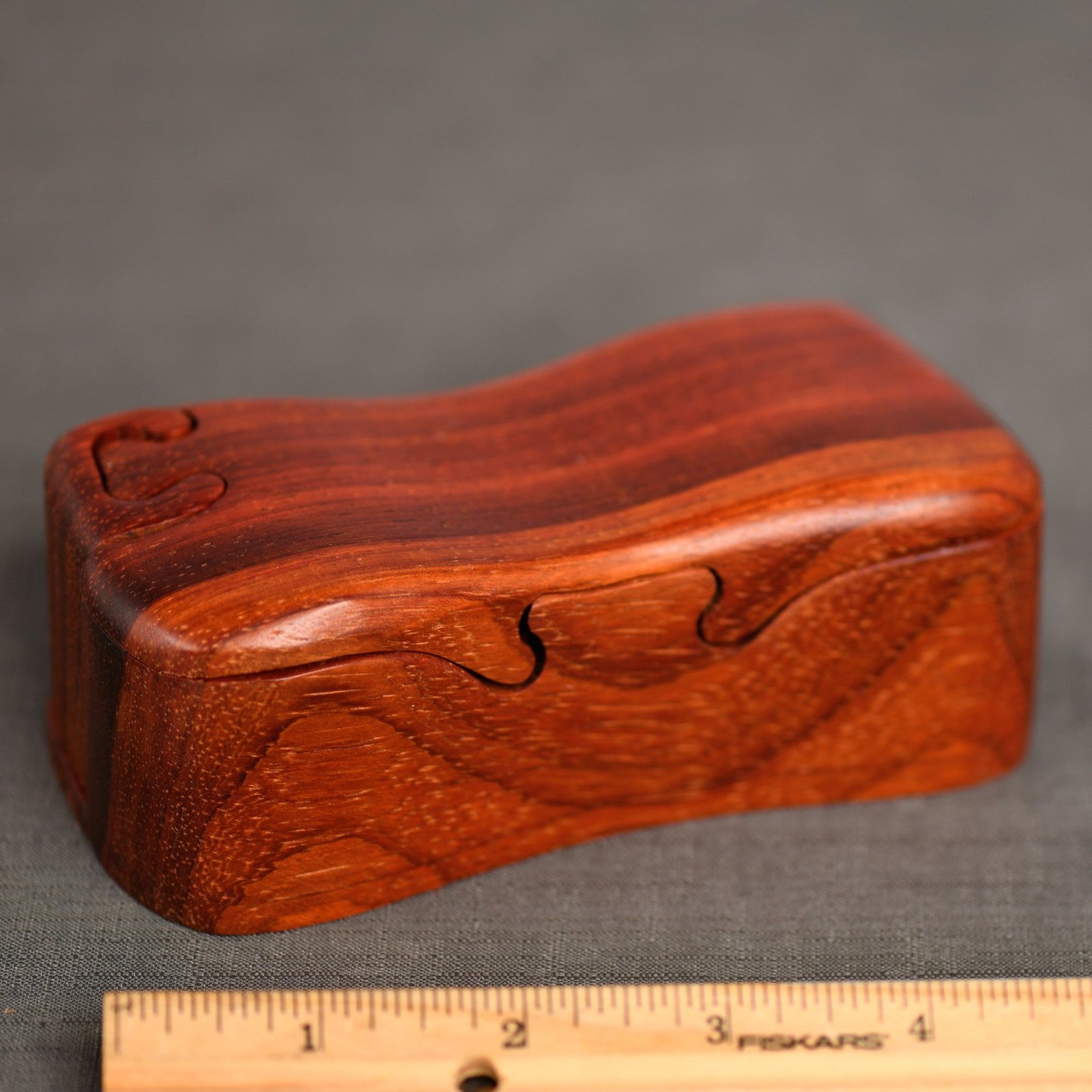 Red-orange padouk bandsawn puzzle box with a ruler for scale, by Designs by Baerreis